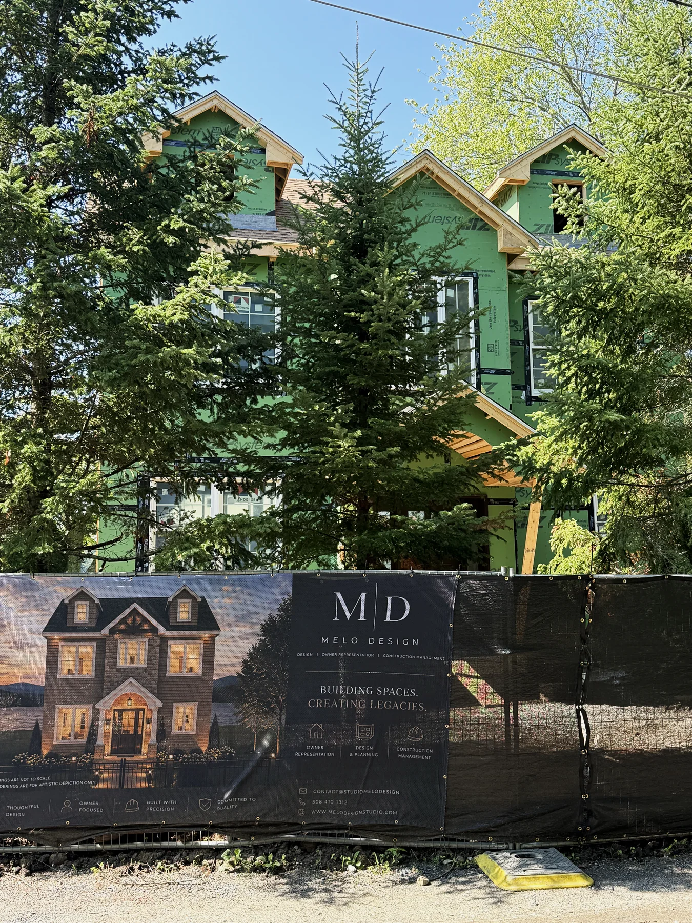 Framed house behind a jobsite banner showing its own rendering